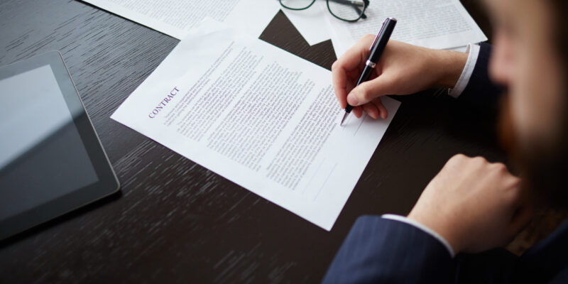 Image of businessman hand with pen signing contract at workplace