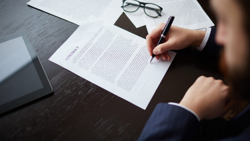 Image of businessman hand with pen signing contract at workplace